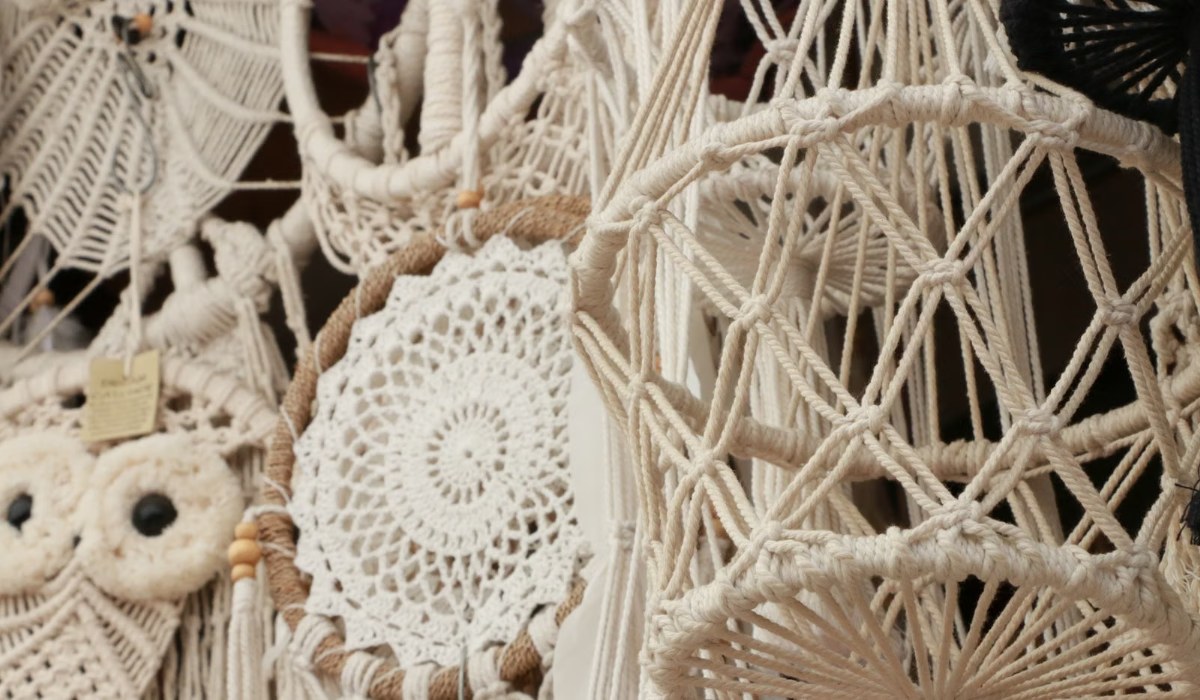 Bedroom wall styled with a woven macrame wall hanging above a bed with layered textiles