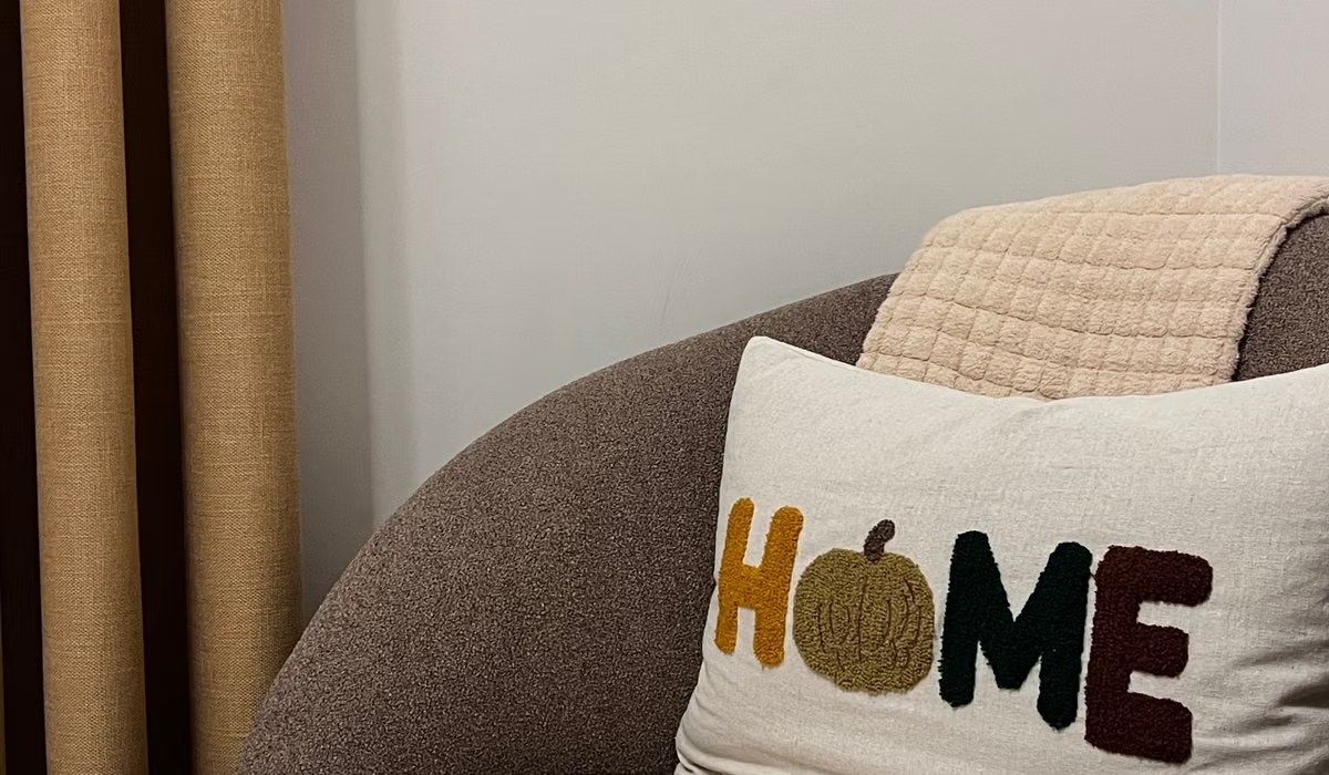 Cozy fall living room with a knit throw, HOME pillow and a small pumpkin on a gray sofa