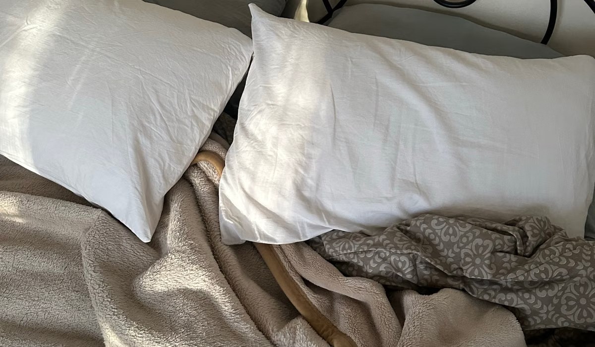 Bed layered with white pillows, a beige textured blanket and a patterned throw