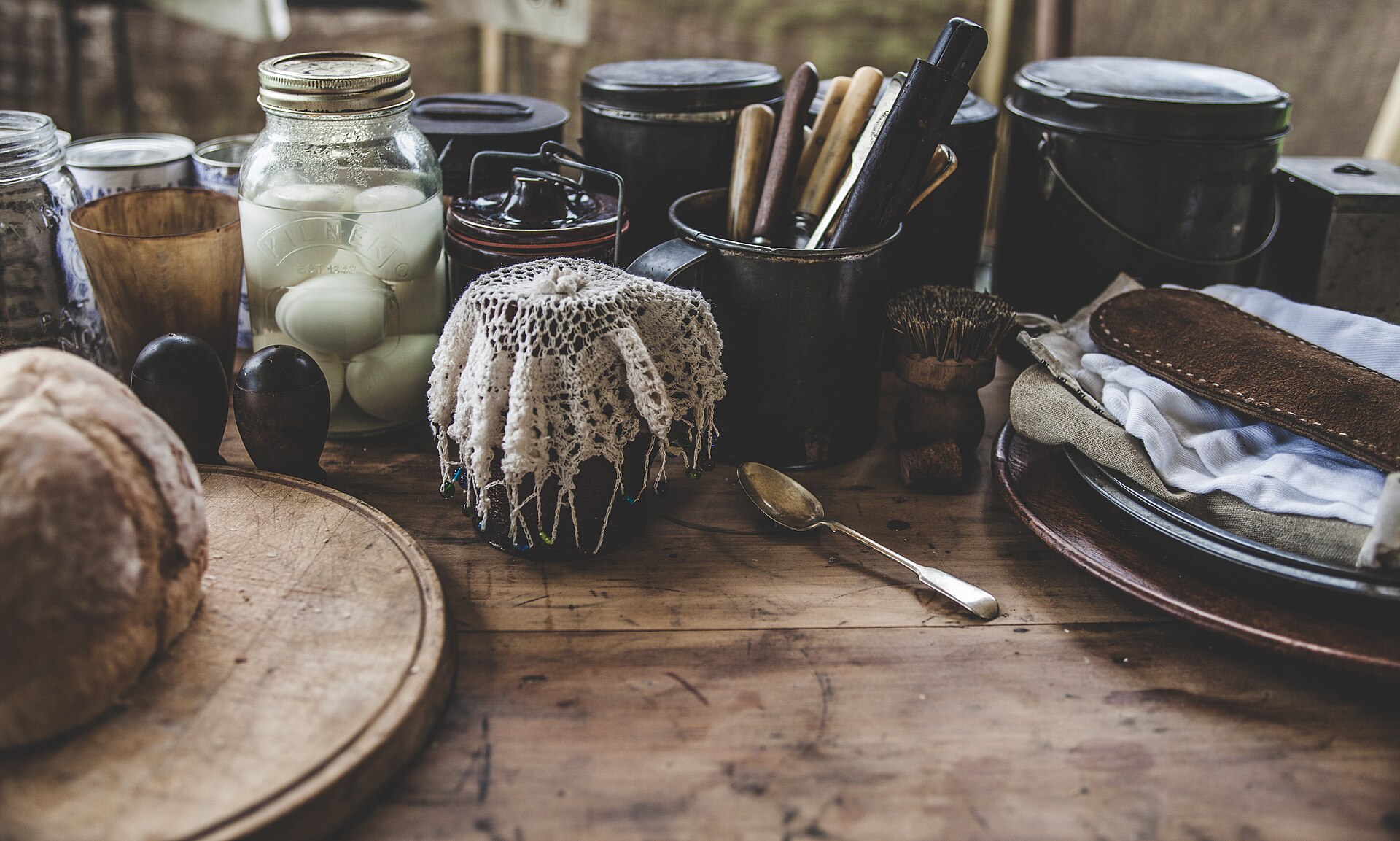 Rustic wooden kitchen table with fresh bread, jars and utensils