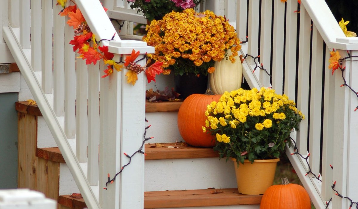 Fall porch railing wrapped in maple leaf garland with mums and pumpkins on the steps