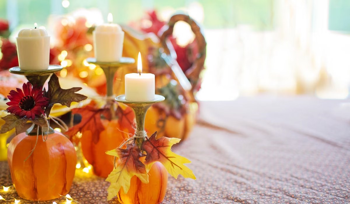 Warm fall table decor with taper candles, small pumpkins and autumn leaves