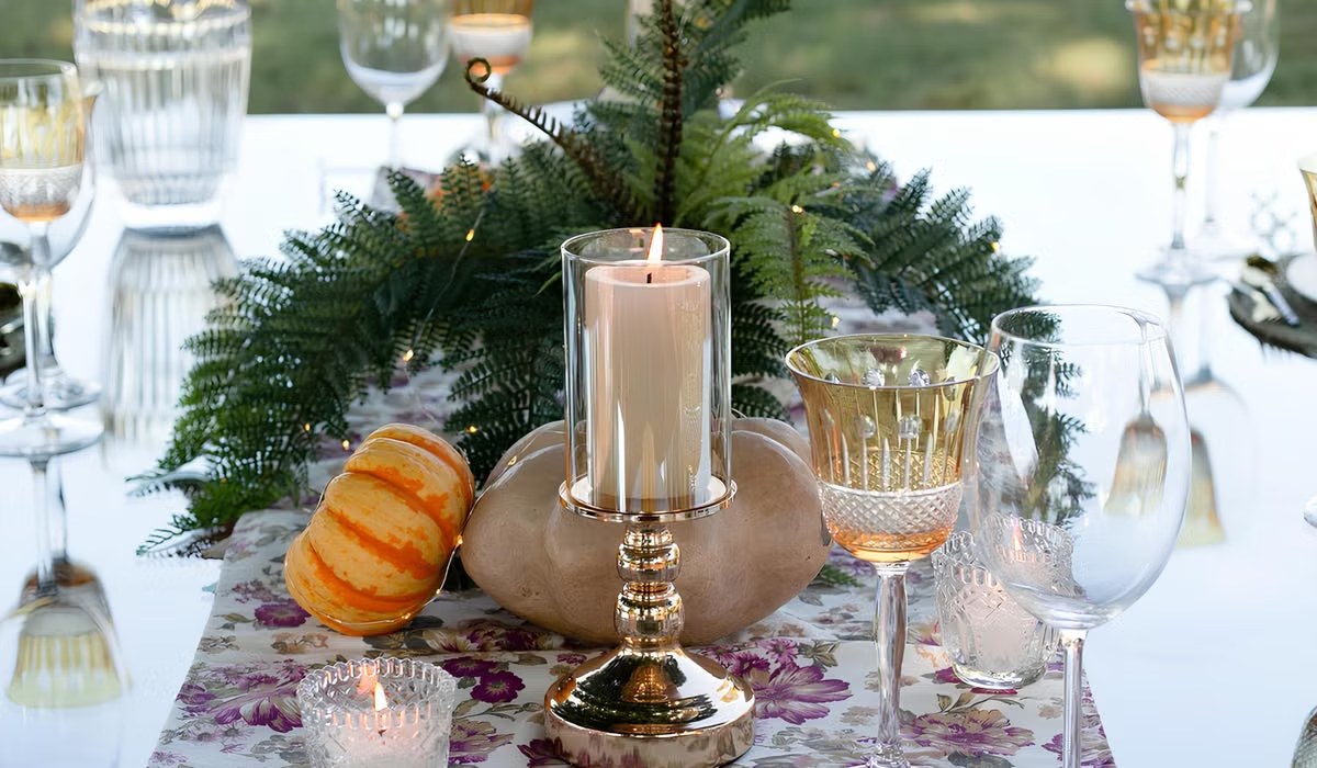 Fall tablescape with evergreen garland runner, mini pumpkins and a hurricane candle
