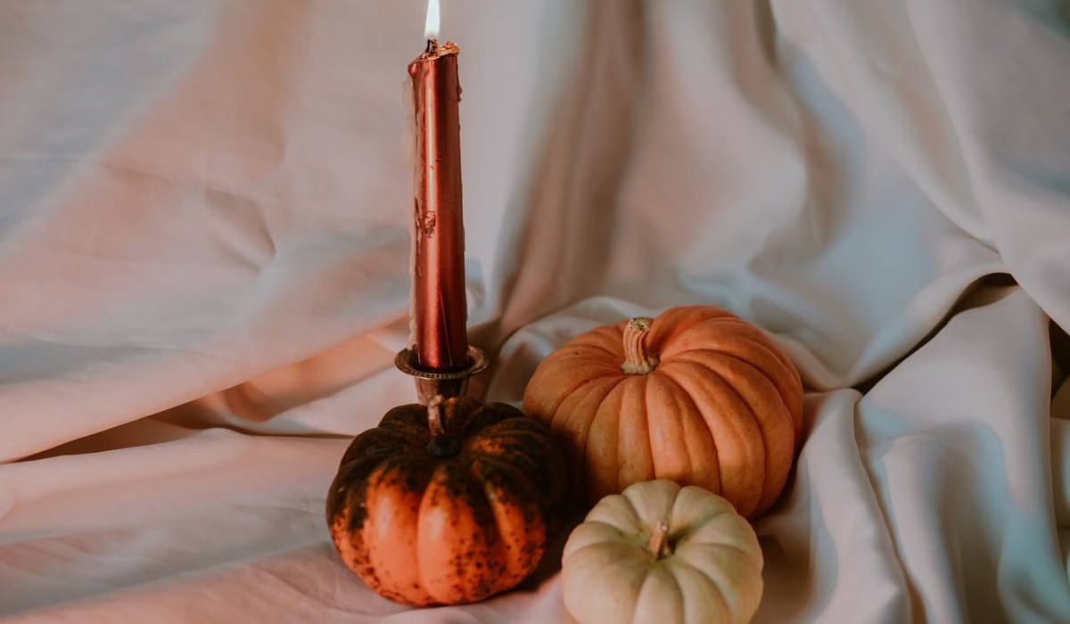 Pumpkins and a lit taper candle styled on soft linen for a cozy Halloween mantel