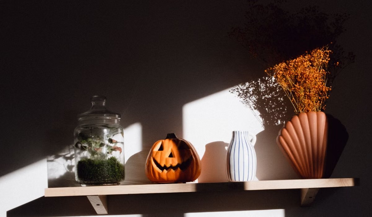A shelf styled with a glowing jack-o-lantern, glass jars and ceramic vases in warm evening light