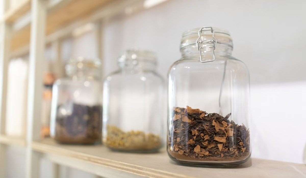 Glass jars filled with dried herbs on a wooden kitchen shelf