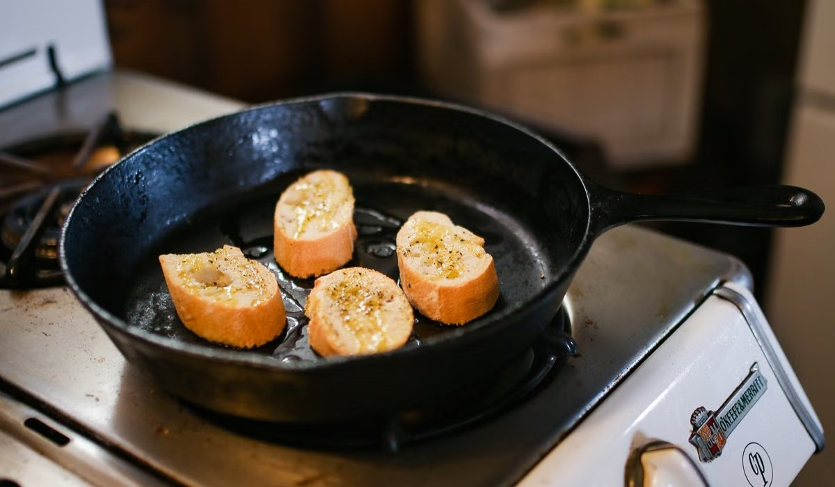 Slices of bread toasting in a cast iron skillet on a stove