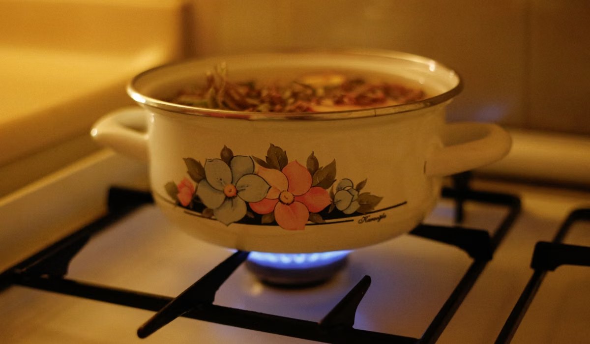 A lidded enamel pot simmering soup on a gas stove